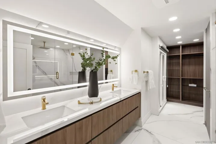 A spa inspired primary bath blending warm wood cabinetry, oversized illuminated mirrors, and refined modern finishes, complete with a boutique-style walk in closet and a serene atmosphere designed for daily retreat.