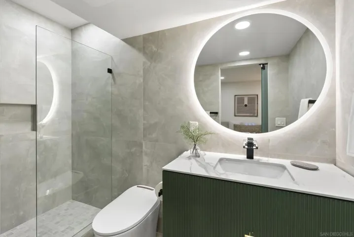 A beautifully appointed en-suite guest bath featuring soft stone finishes, a backlit circular mirror, and sleek modern detailing that creates a refined, spa inspired atmosphere.