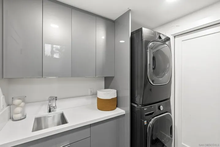 A sleek and functional laundry room featuring custom cabinetry, stacked washer and dryer appliances, and clean contemporary finishes designed to elevate everyday convenience.