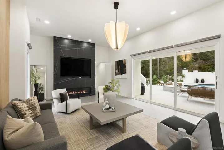 A striking formal living room designed for refined entertaining, where soaring ceilings, dramatic fireplace surrounded by sleek stone, and walls of glass create a sophisticated atmosphere with a seamless connection to the outdoor terrace.