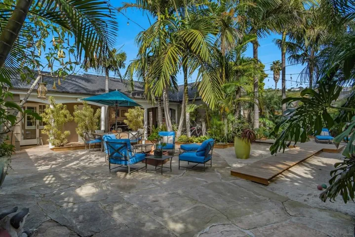 A private tropical courtyard designed for effortless entertaining, where layered palms, natural stone, and sunlit lounge spaces create a serene indoor outdoor retreat in the heart of La Jolla.