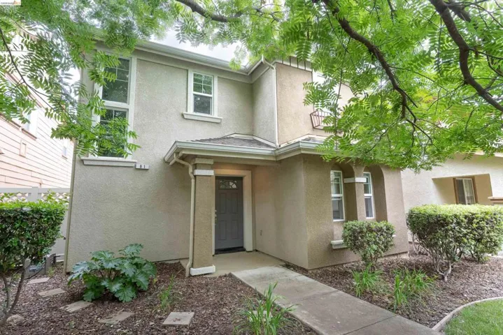 Stucco exterior featuring a covered entry, established landscaping with stepping stones, an arched window detail, and multiple windows across two levels