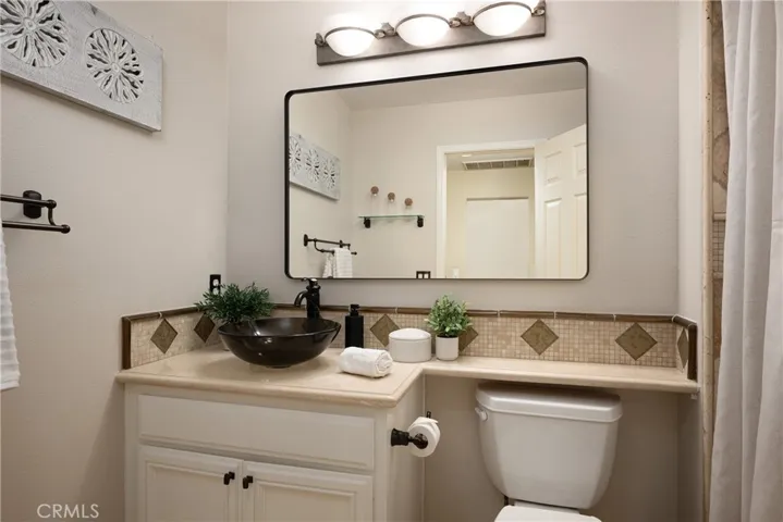 Down the hall is an upgraded guest bathroom featuring a glass bowl sink, travertine flooring, and beautiful countertops.
