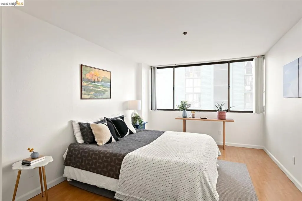 Bright interior room featuring a large window with roller shades, light wood-finish flooring, and white walls