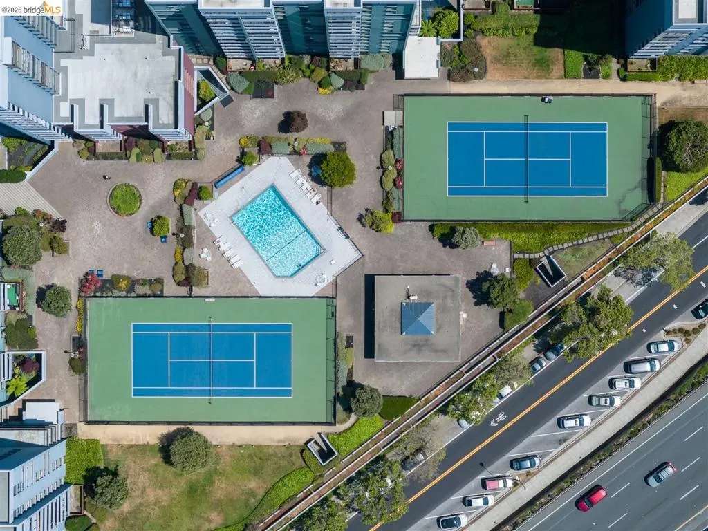 Aerial view showcasing two tennis courts, a swimming pool, and landscaped common areas