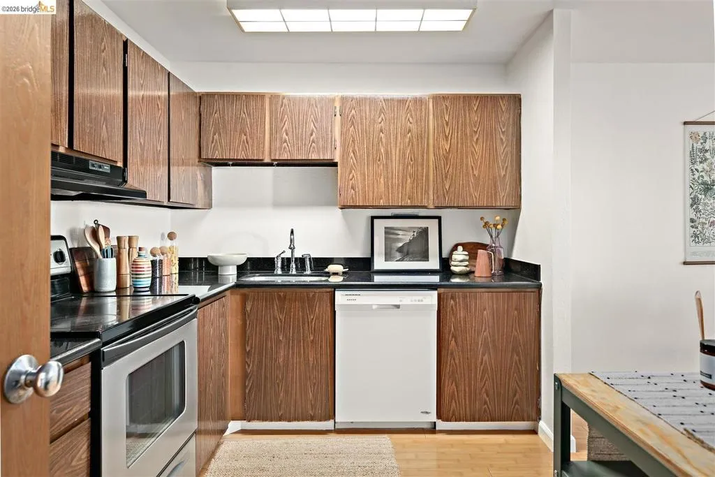 Compact kitchen featuring wood-finish cabinetry, black countertops, and a stainless steel oven