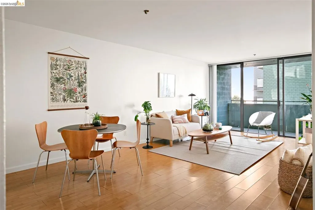 Open-concept living space featuring wood-finish flooring, a dining area with a dark tabletop, a living room with light-colored walls, and a sliding glass door opening to a private balcony