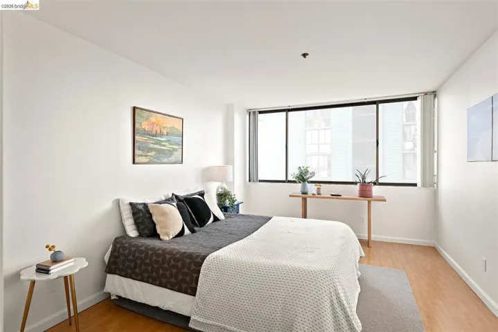 Bright interior room featuring a large window with roller shades, light wood-finish flooring, and white walls