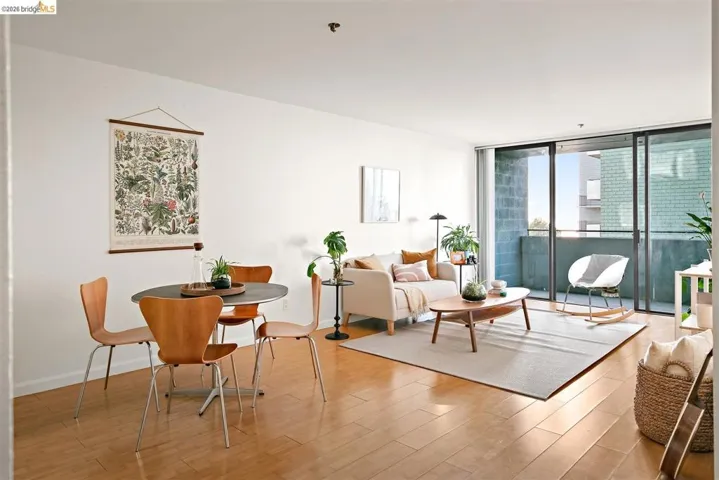 Open-concept living space featuring wood-finish flooring, a dining area with a dark tabletop, a living room with light-colored walls, and a sliding glass door opening to a private balcony