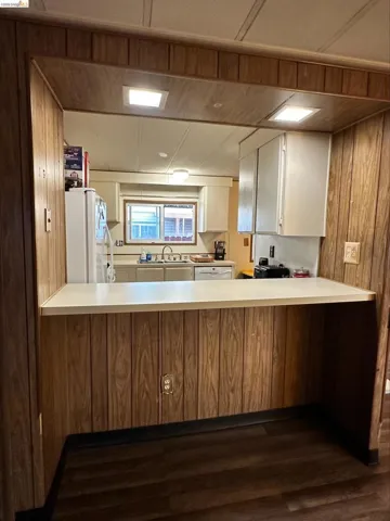 Kitchen with wood walls, light countertops, white appliances, white cabinets, and dark wood-style flooring