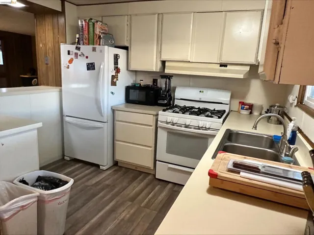 Kitchen with white appliances, light countertops, dark wood-style floors, and under cabinet range hood