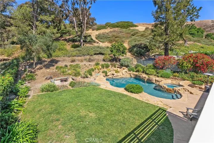 Looking down on beautiful backyard and green space slopes from primary bedroom balcony. Private pool, spa, fire pit & grassy yard in back.