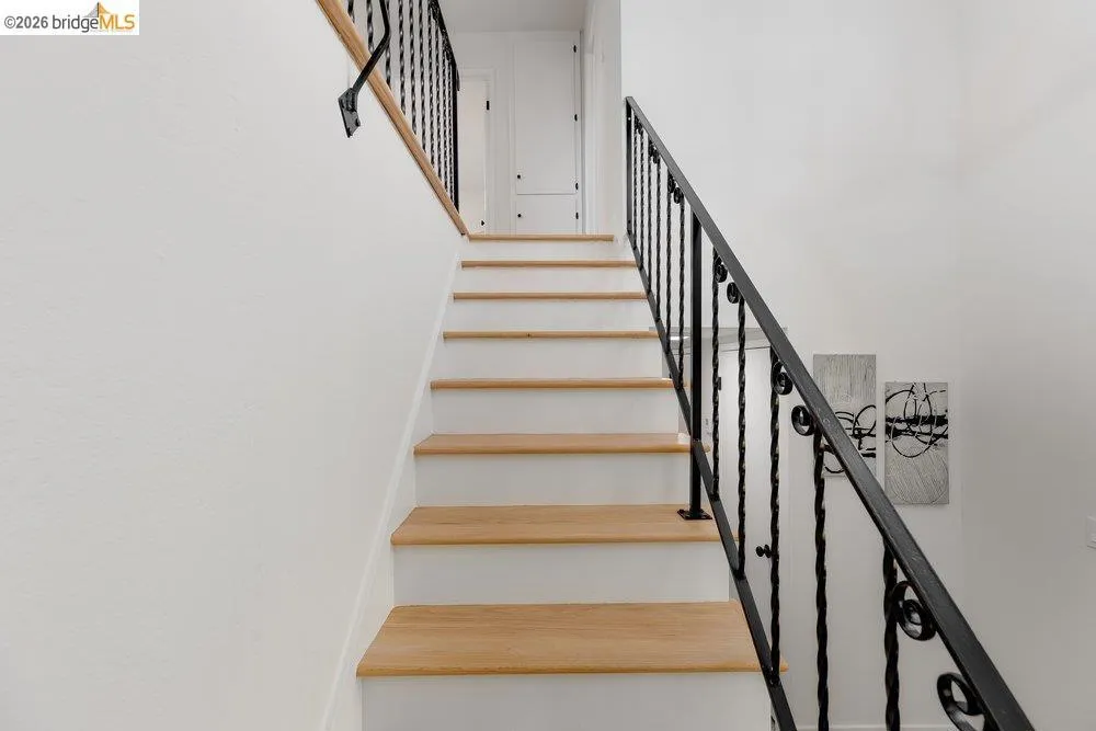 Staircase featuring wood-finish treads, white risers, a wrought iron balustrade, and a wood handrail