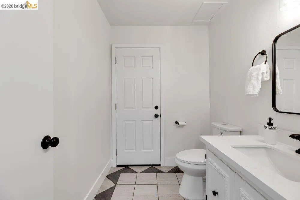 Bathroom featuring a white paneled door, patterned tile flooring, a built-in vanity with white countertop, and a contemporary wall-mounted mirror