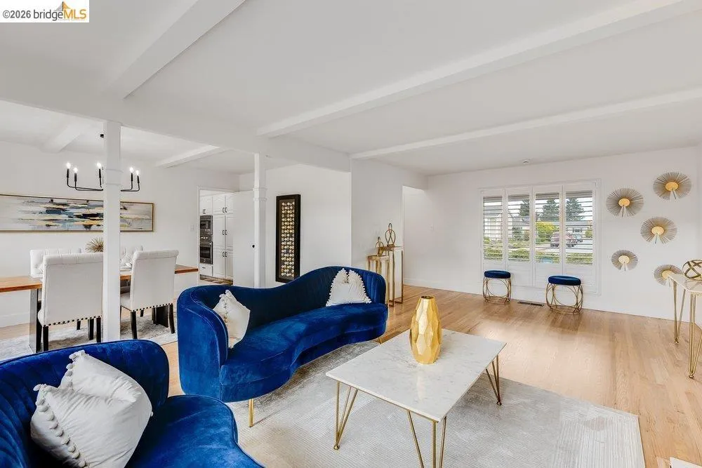 Bright living space featuring natural wood-finish flooring, white walls, and a beamed ceiling