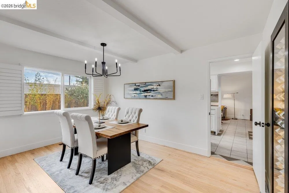Open-concept dining area featuring light wood-finish flooring, white walls, and exposed ceiling beams