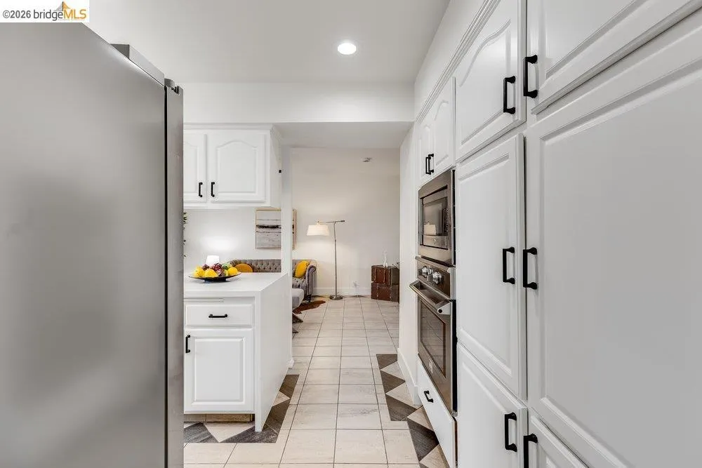 White cabinetry with black hardware, built-in stainless steel appliances, and checkerboard floor tiling