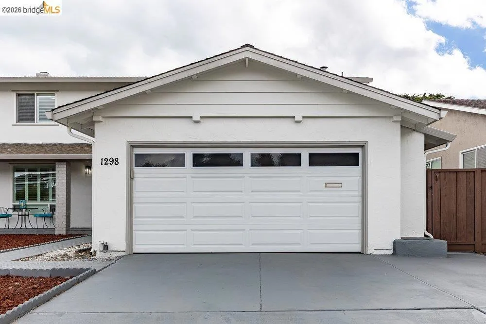 Front exterior featuring a white paneled garage door with upper window inserts, a painted concrete driveway, and stucco siding