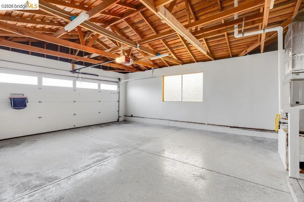 Garage with exposed wood beam ceiling, white walls, frosted glass window, and concrete flooring