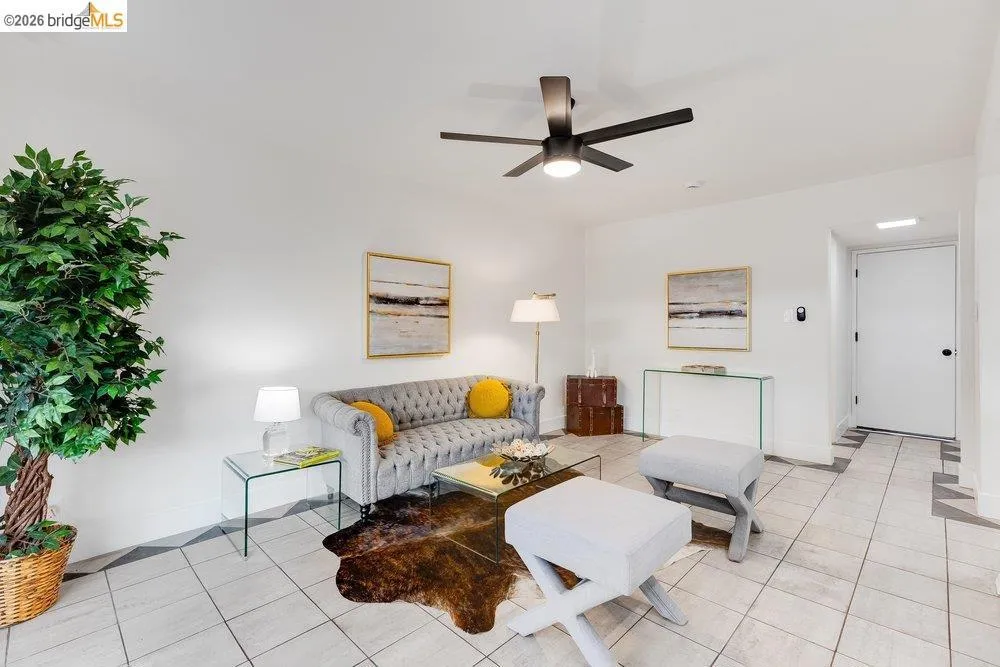 Spacious living area featuring light-toned tile flooring with geometric accents, a contemporary ceiling fan, and white walls