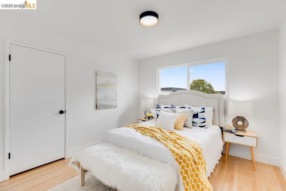 Bright bedroom featuring light wood-finish flooring, white walls, and a modern ceiling light fixture