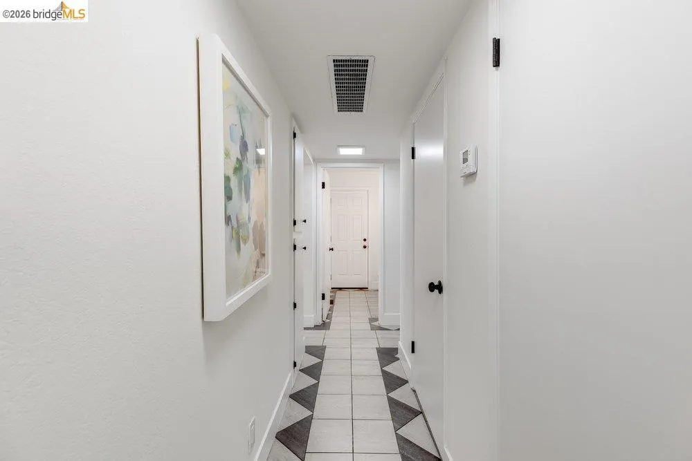 Hallway featuring light-toned walls, tile flooring with a geometric pattern, and multiple white doors with matte black hardware