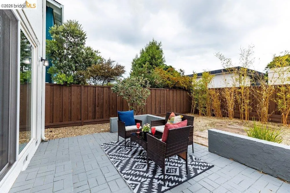 Spacious outdoor patio featuring a patterned paver surface, wood privacy fencing, and a built-in planter