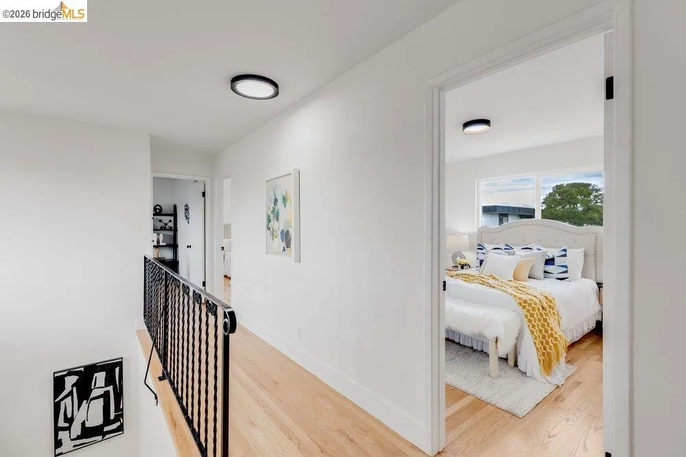 Bright hallway featuring light wood-finish flooring, white walls, and a black wrought iron​​‌​​​​‌​​‌‌​​‌​​​‌‌​​​‌​​‌‌​​‌‌​​‌‌​​​​ railing