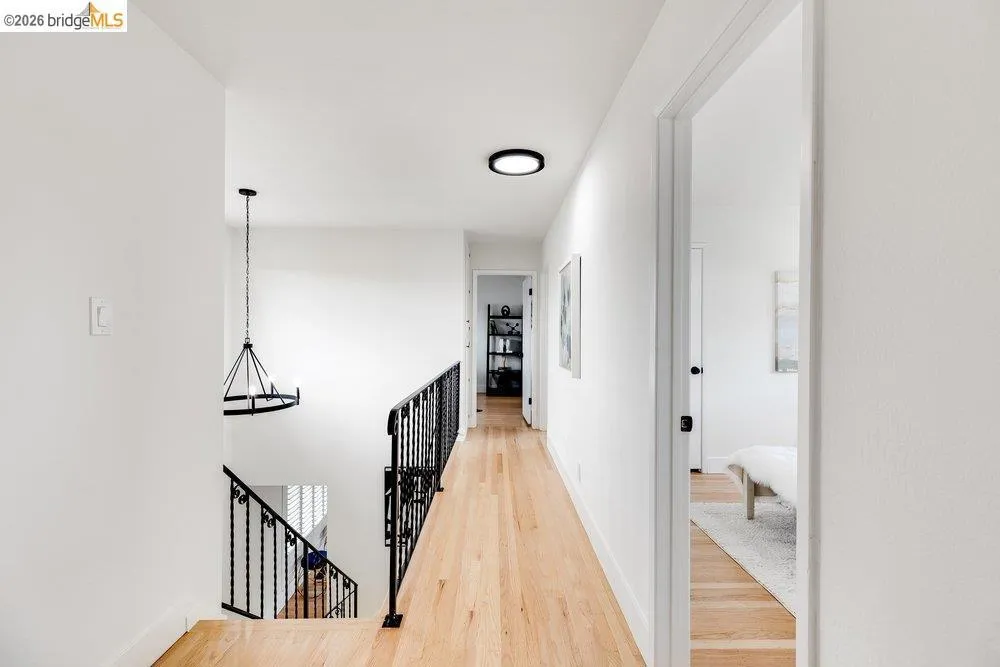 Upper-level hallway featuring wood-finish flooring, white walls, and contemporary ceiling light fixtures