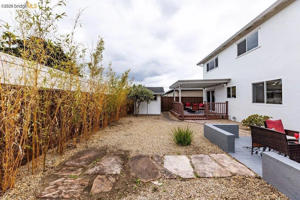 Expansive gravel backyard featuring natural stone pavers, a privacy fence with bamboo plantings, and a raised wooden deck with an attached patio cover