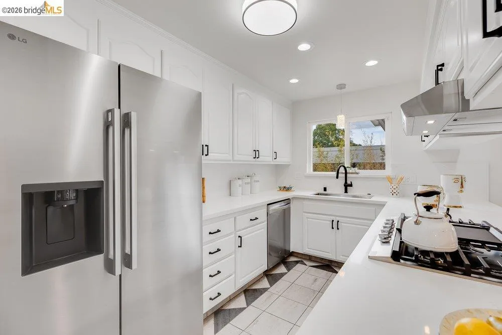 Modern kitchen featuring stainless steel appliances, white cabinetry with black hardware, white countertops, and a distinct black and white floor tile pattern