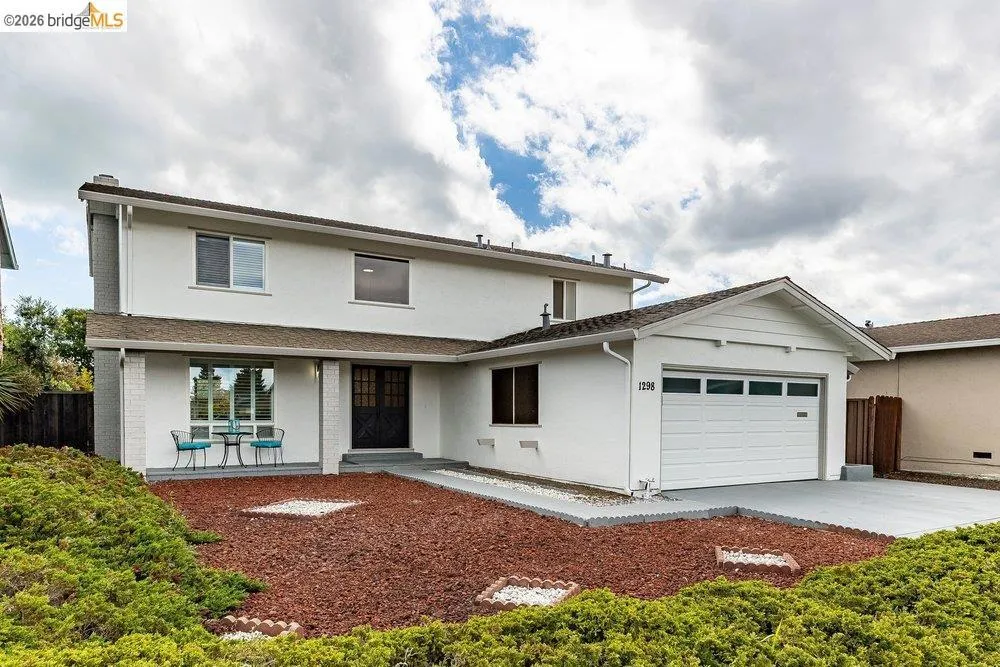 Two-story white stucco residence featuring a covered front porch, an attached garage, a driveway, and a landscaped front yard with ground cover and rock accents