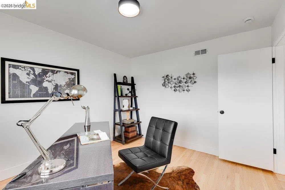 Light wood-finish flooring complements white walls in this room, featuring a solid white door with black hardware, a ceiling-mounted light fixture, and a built-in wall vent