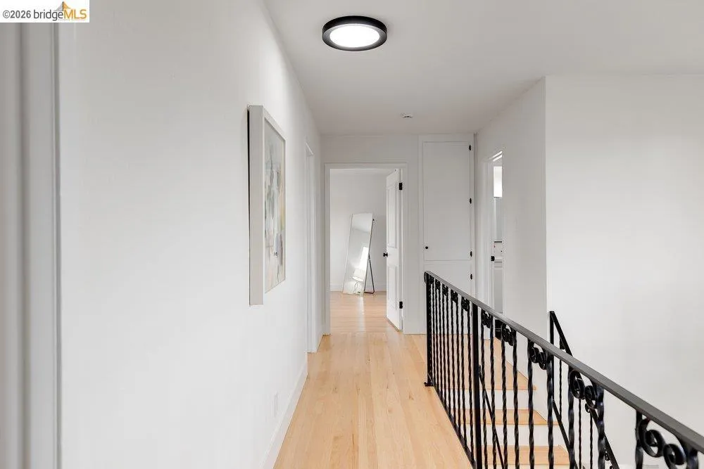 Hallway featuring light wood-finish flooring, white walls, and a black wrought iron stair railing