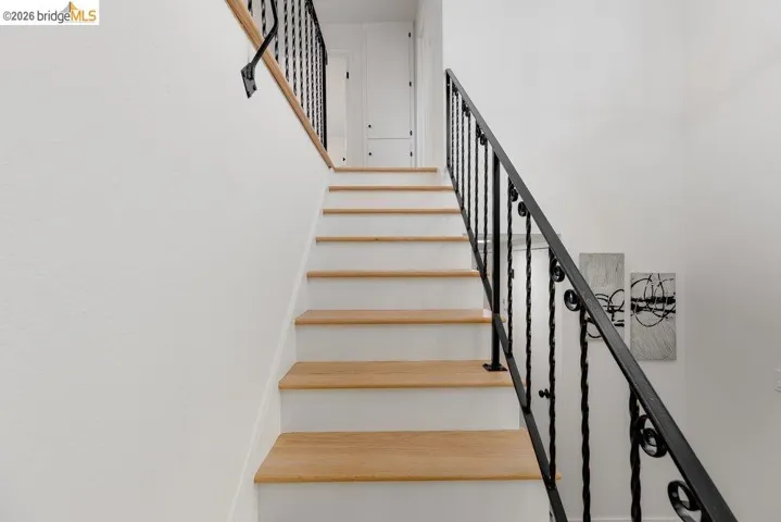 Staircase featuring wood-finish treads, white risers, a wrought iron balustrade, and a wood handrail