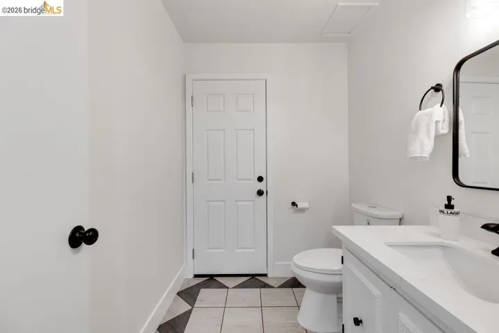 Bathroom featuring a white paneled door, patterned tile flooring, a built-in vanity with white countertop, and a contemporary wall-mounted mirror