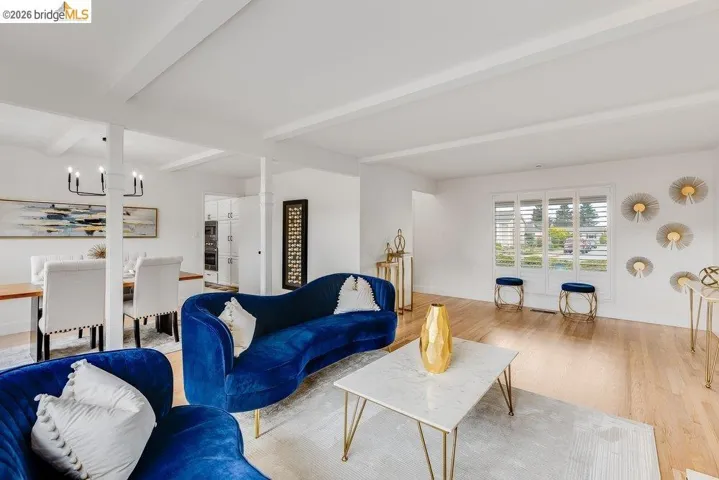 Bright living space featuring natural wood-finish flooring, white walls, and a beamed ceiling