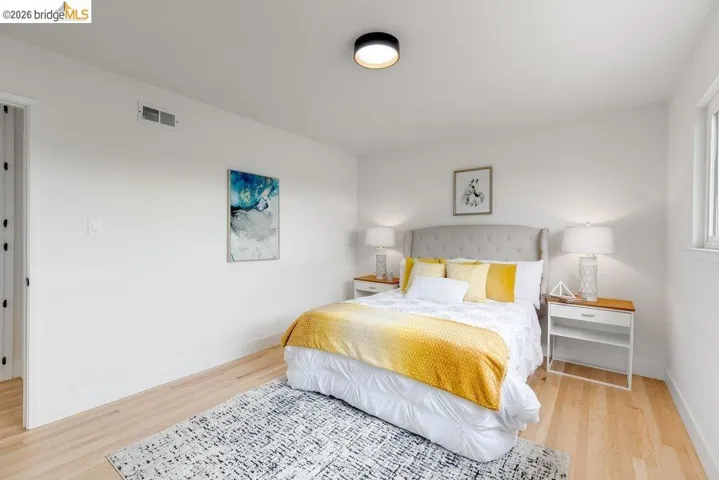 Bright bedroom featuring light wood-finish flooring, white walls, a single window, and a modern ceiling light fixture