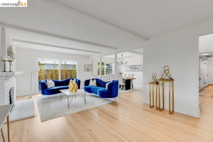 Bright living area featuring wood-finish flooring, a white brick fireplace with a tile hearth, and ceiling beams