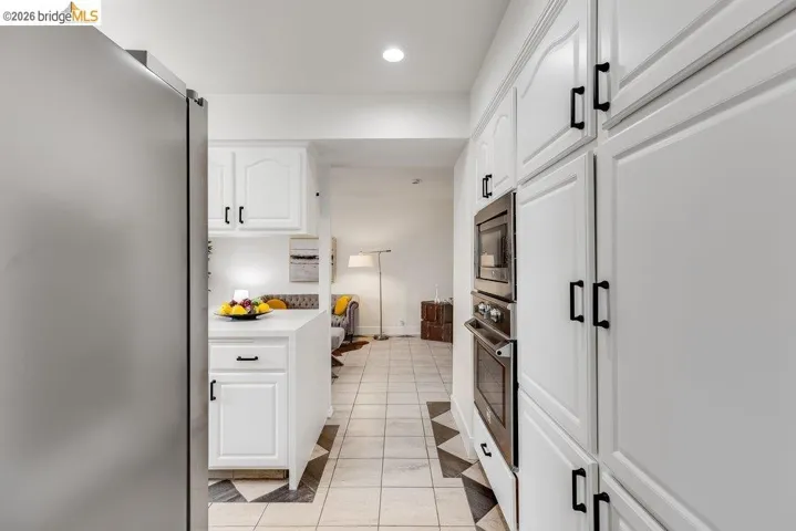 White cabinetry with black hardware, built-in stainless steel appliances, and checkerboard floor tiling