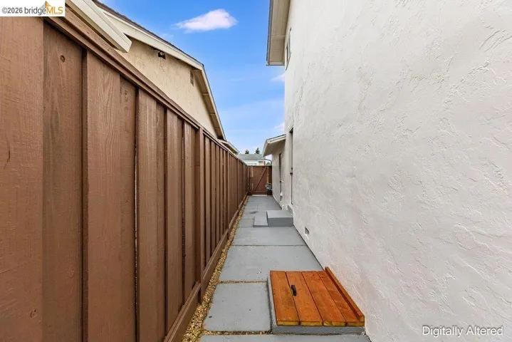 Side yard featuring a privacy fence, stucco exterior, concrete pathway, and steps to a rear door