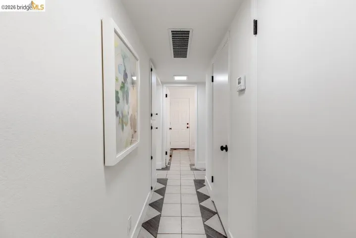 Hallway featuring light-toned walls, tile flooring with a geometric pattern, and multiple white doors with matte black hardware