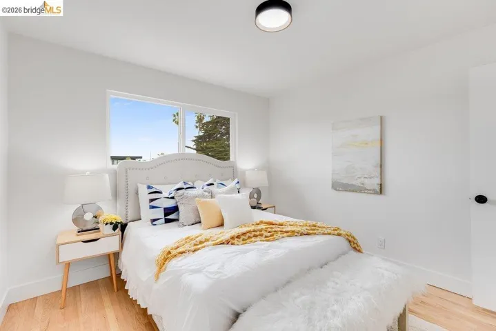 Bright bedroom with light wood-finish flooring, white walls, and a large window