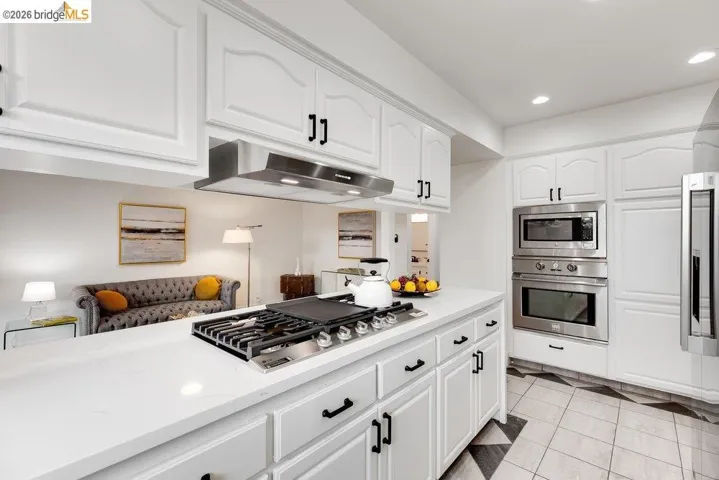 Kitchen featuring white cabinetry with black hardware, white countertops, a gas range with a stainless steel vent hood, and stainless steel built-in double ovens