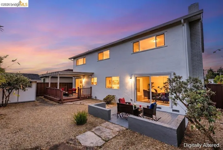 Rear exterior featuring a spacious gravel yard with stone stepping paths, a wood deck with railings, and a covered patio area