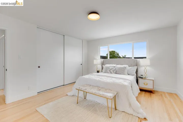 Bright bedroom featuring light wood-finish flooring, a large window, a ceiling-mounted light fixture, and white sliding closet doors