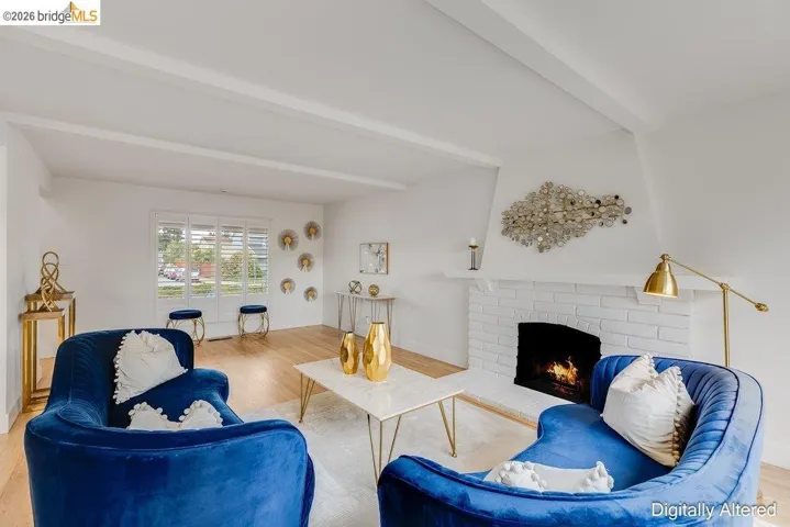 Living space featuring a whitewashed brick fireplace, wood-finish flooring, and exposed ceiling beams
