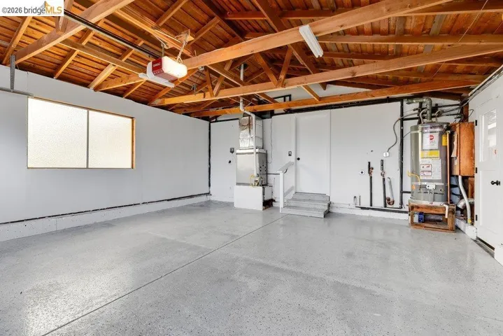 Spacious garage featuring an exposed beam ceiling, concrete flooring, and a large frosted window