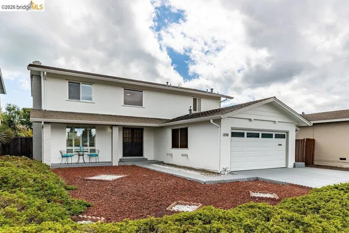 Two-story white stucco residence featuring a covered front porch, an attached garage, a driveway, and a landscaped front yard with ground cover and rock accents
