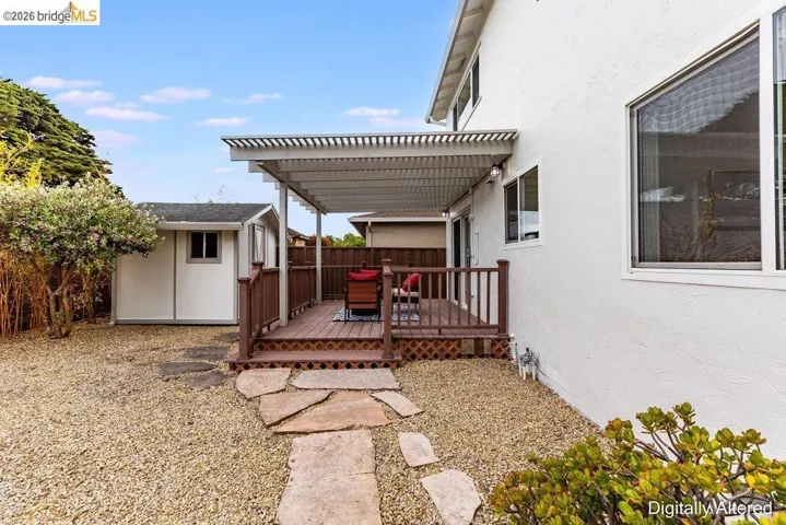 Outdoor deck with slatted pergola, featuring wood railing and stone pathway